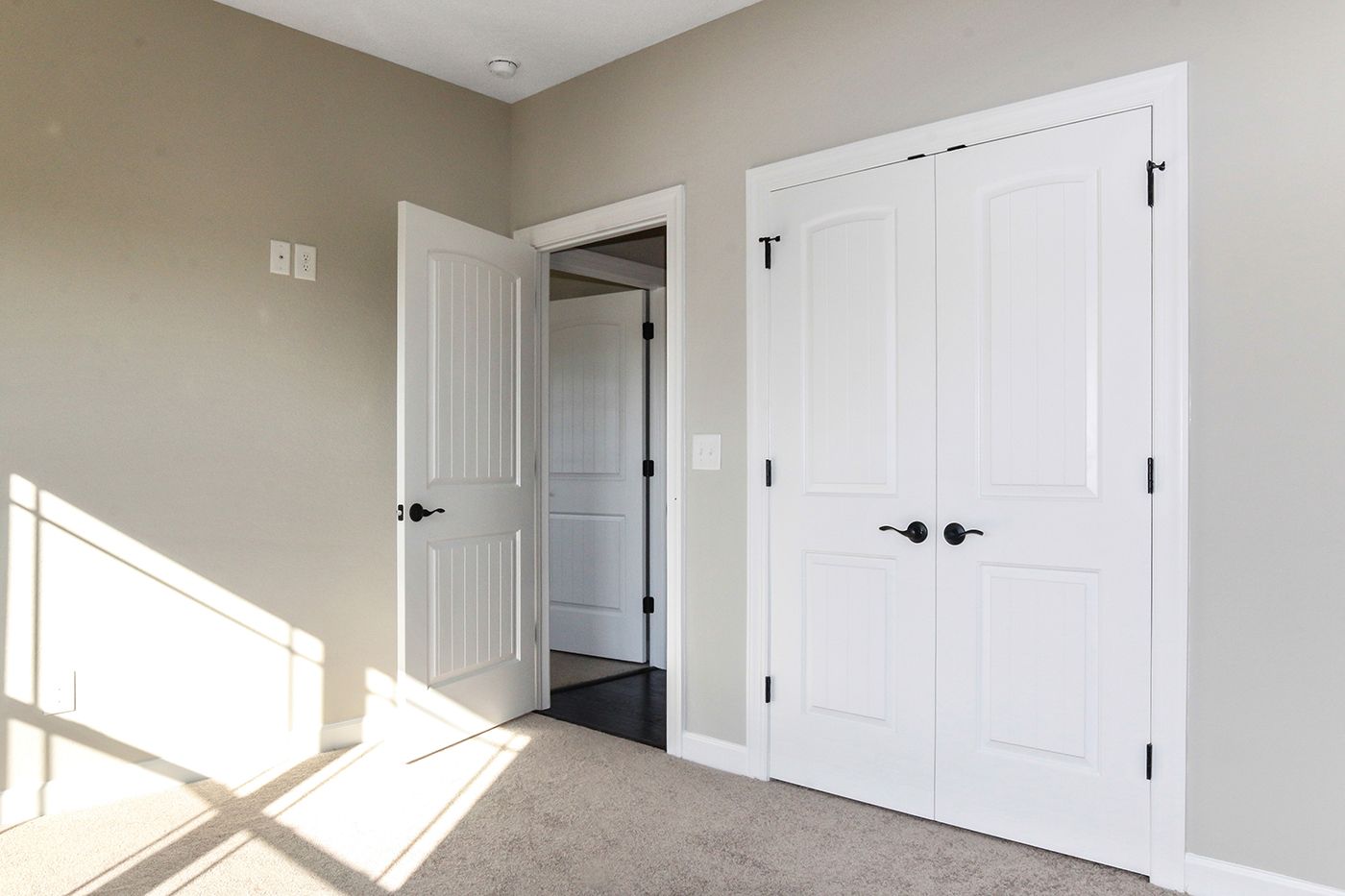 An empty bedroom with white doors and a carpeted floor.