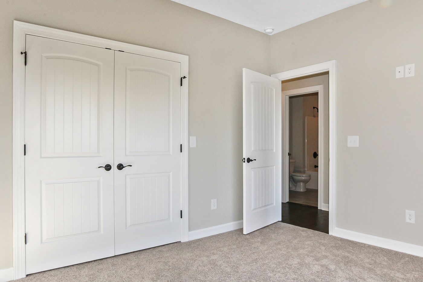 An empty bedroom with two white doors and a toilet.