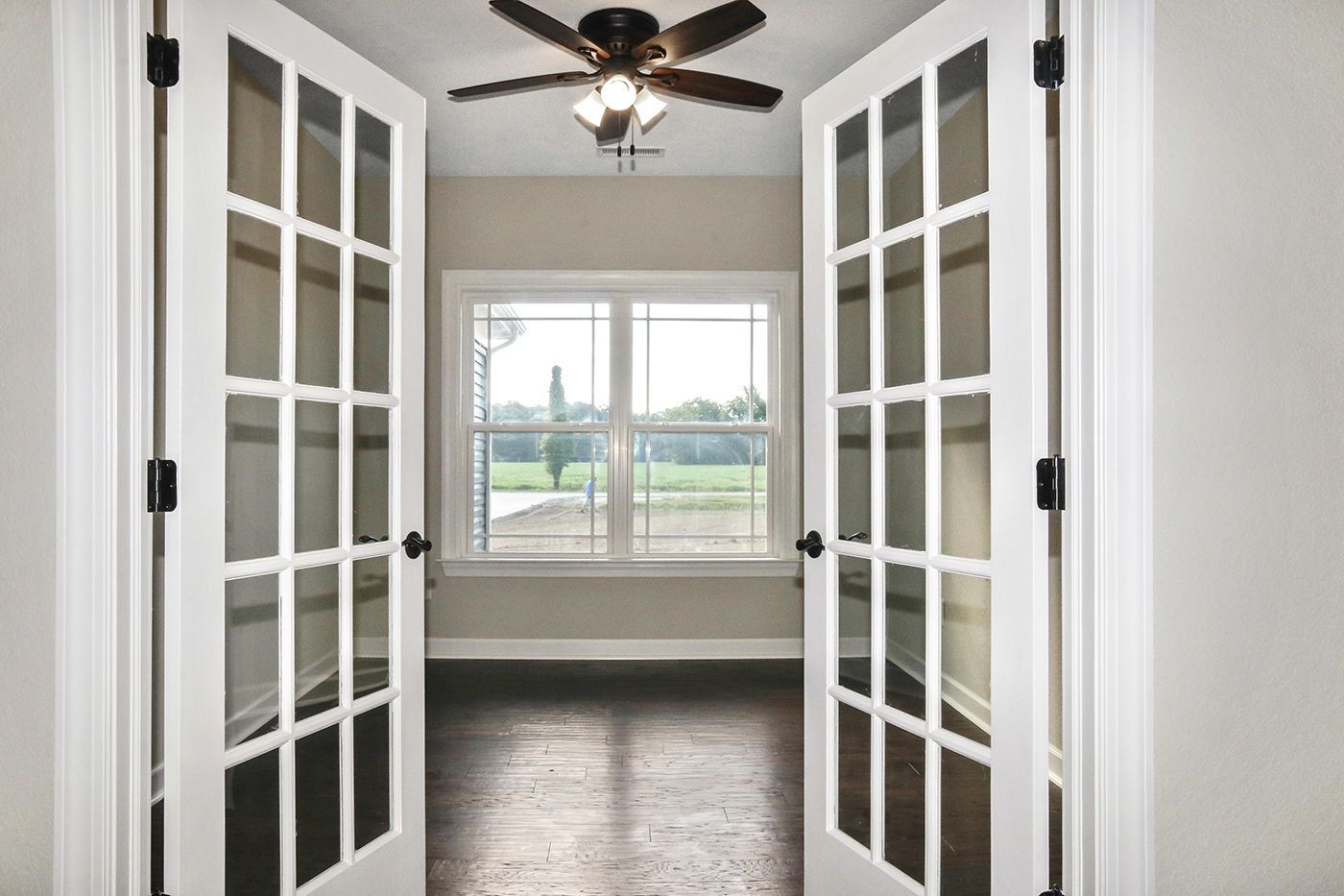 An empty room with french doors and a ceiling fan.