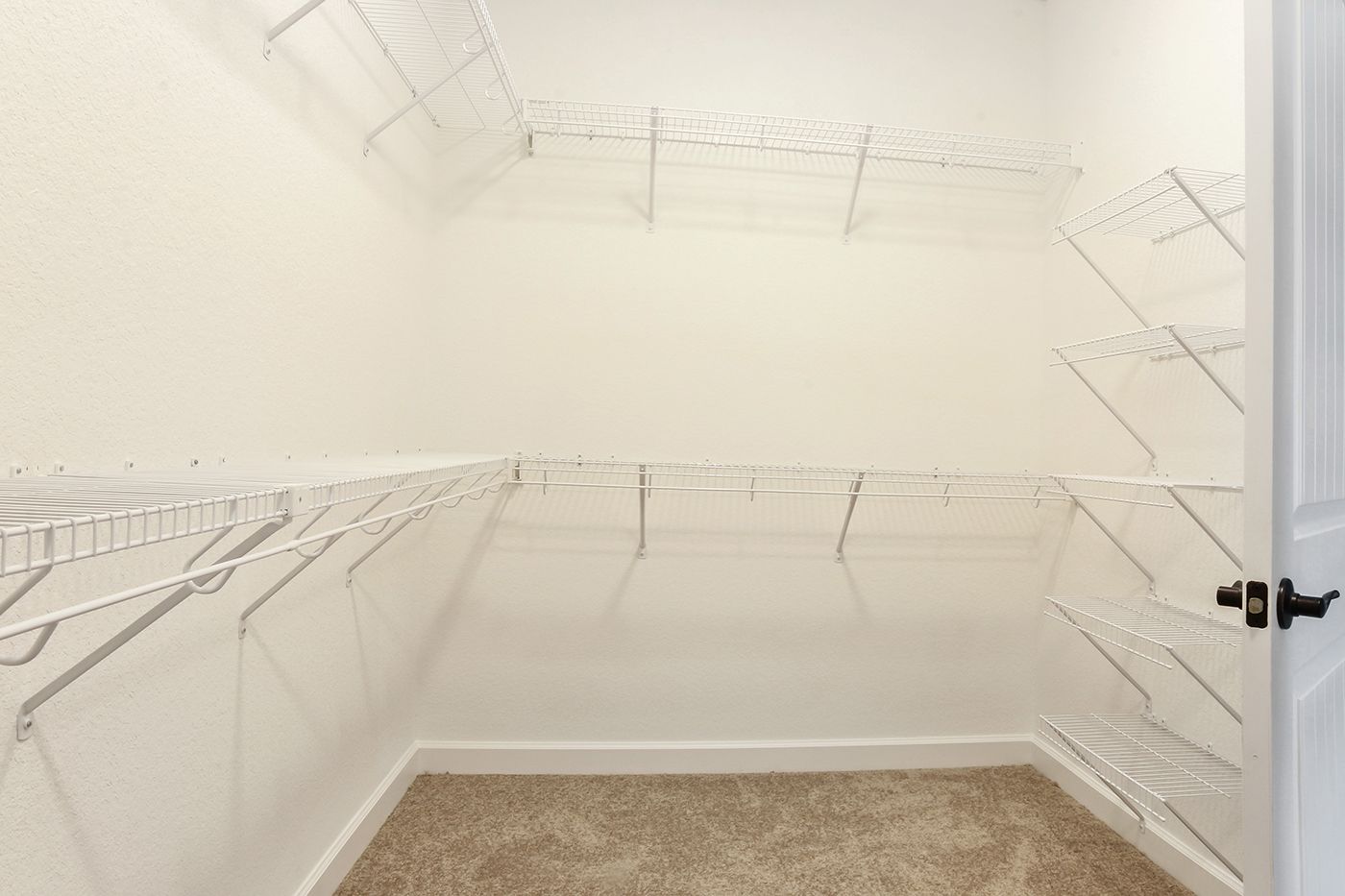 An empty walk in closet with lots of shelves and a door.