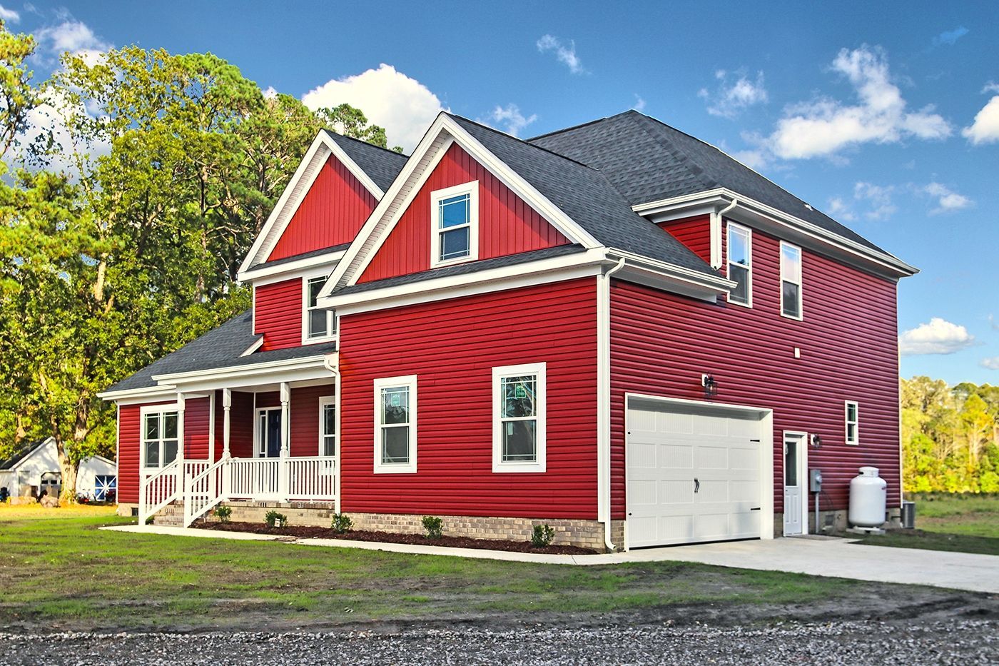 A red house with a white garage door is sitting on top of a lush green field.