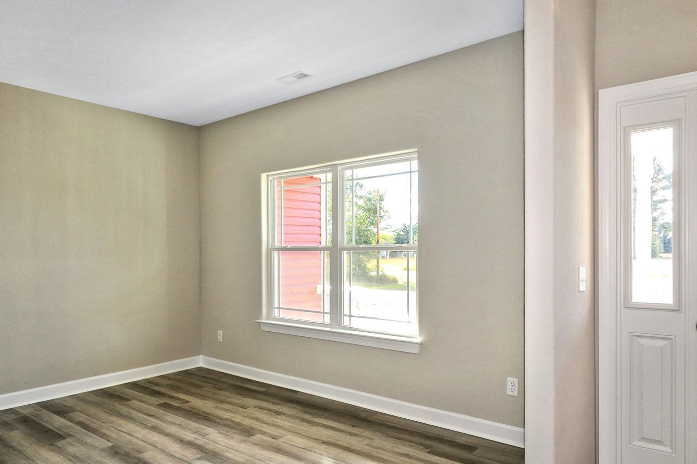 An empty living room with hardwood floors and two windows.
