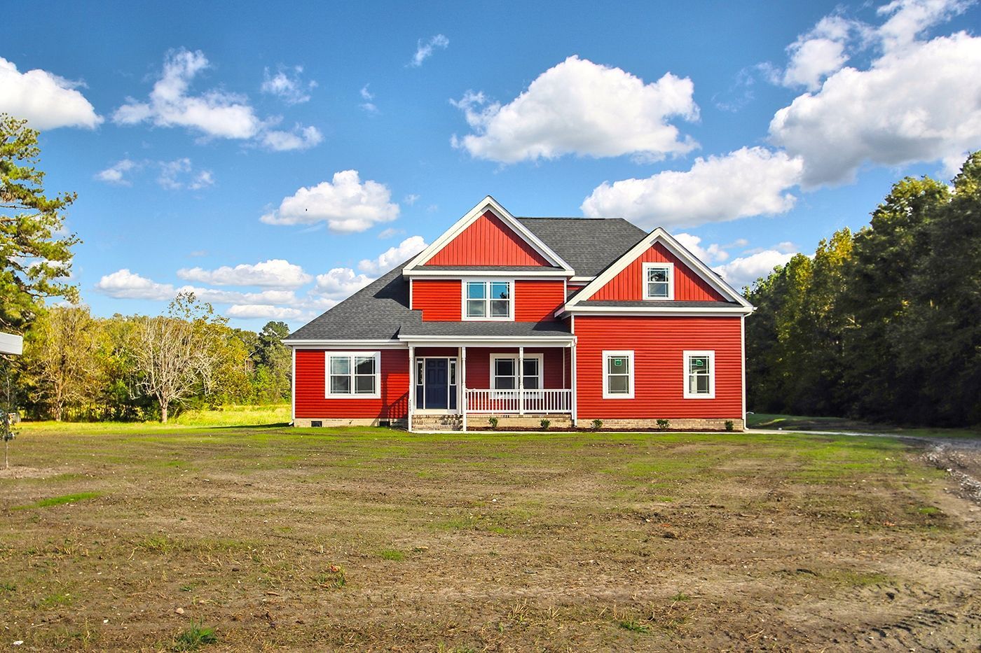 A red house with white trim sits in the middle of a grassy field