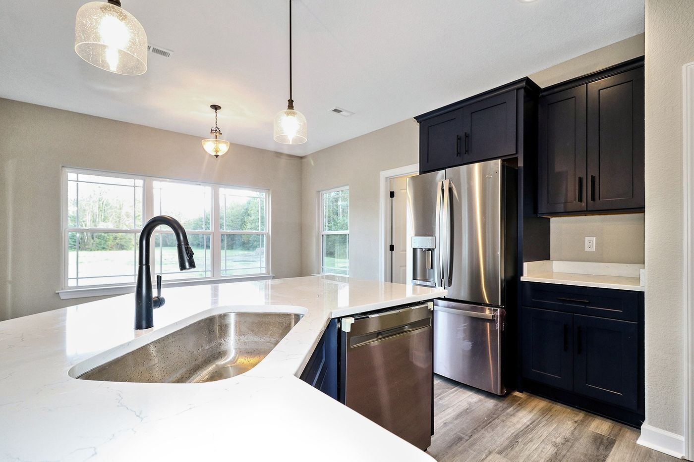 A kitchen with a sink , refrigerator , dishwasher , and black cabinets.