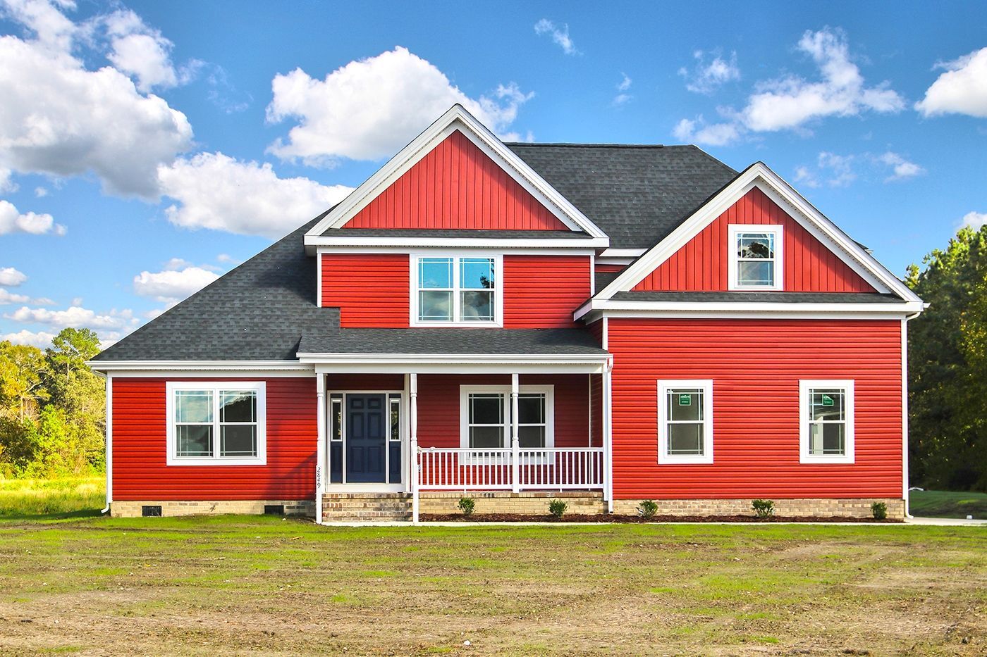 A large red house with a black roof is sitting on top of a lush green field.