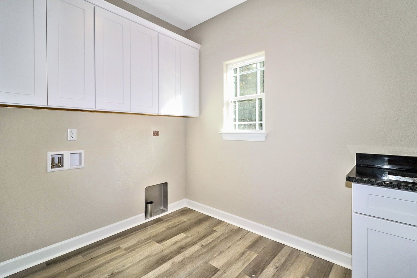 A laundry room with hardwood floors , white cabinets and a window.
