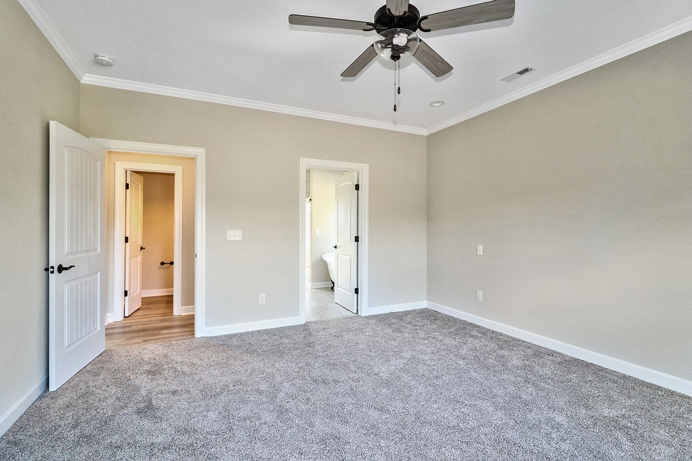 An empty bedroom with a ceiling fan and a carpeted floor.