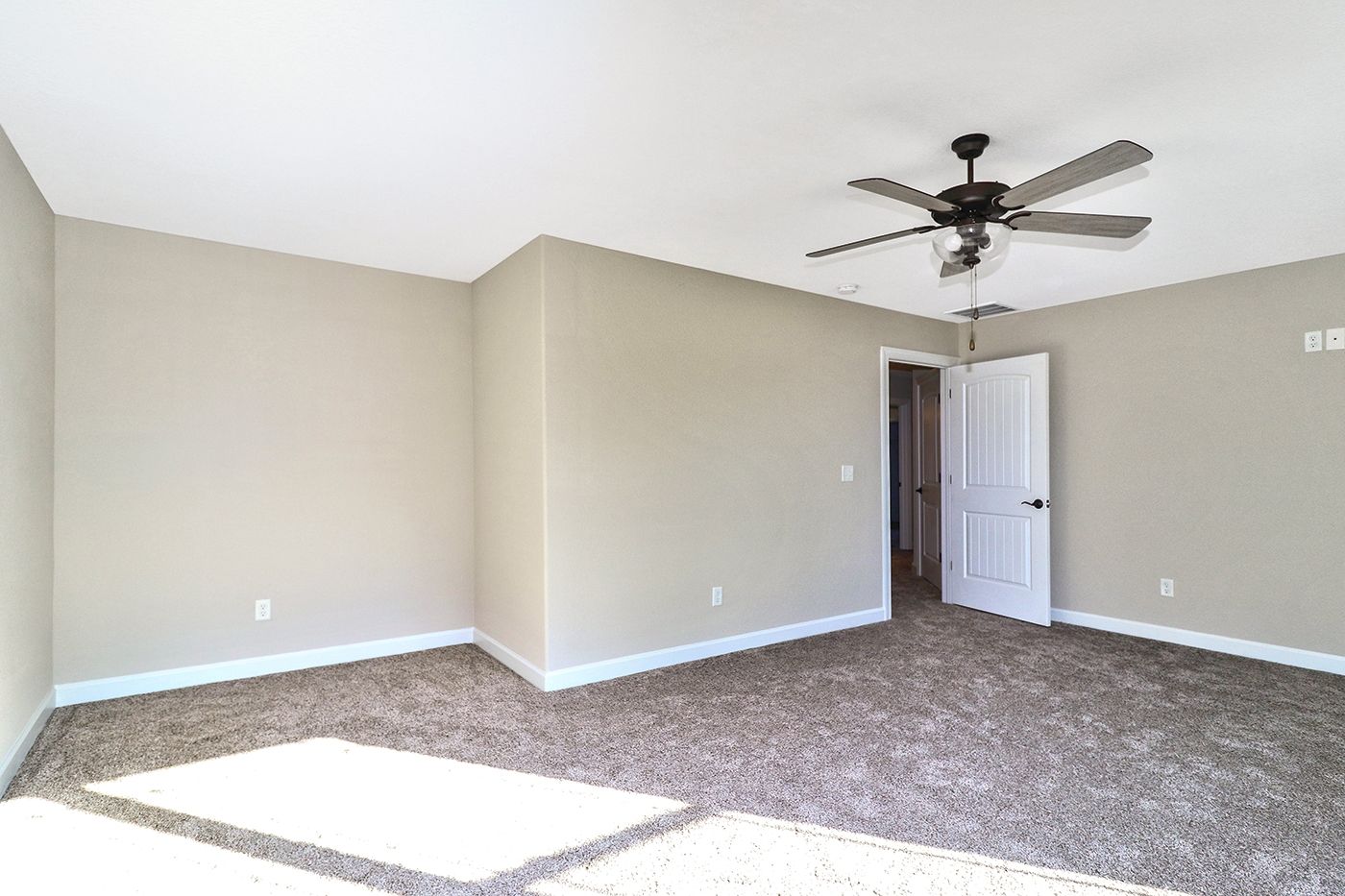 An empty bedroom with a ceiling fan and a door.