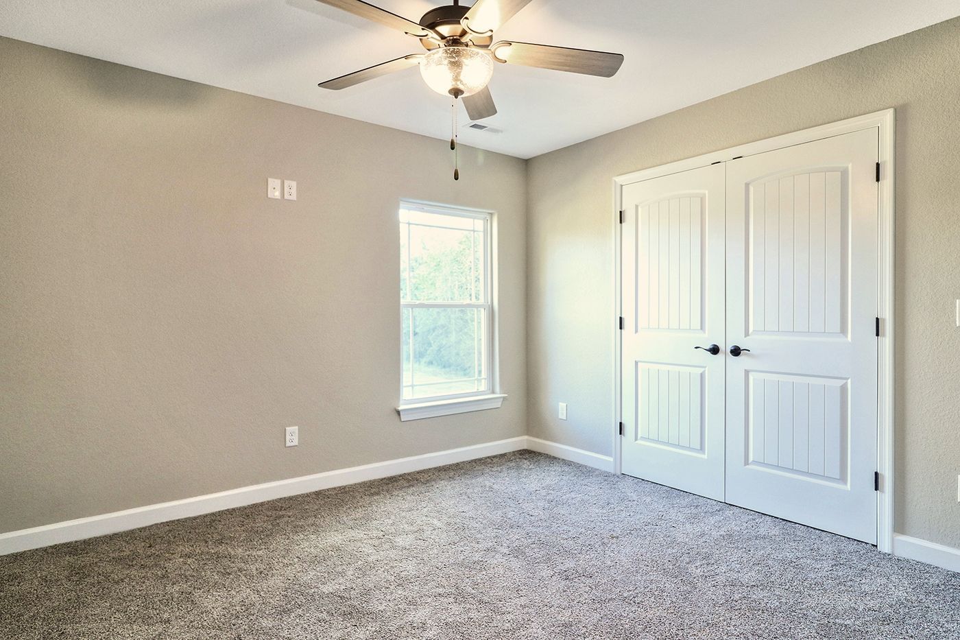 An empty bedroom with a ceiling fan and a window.