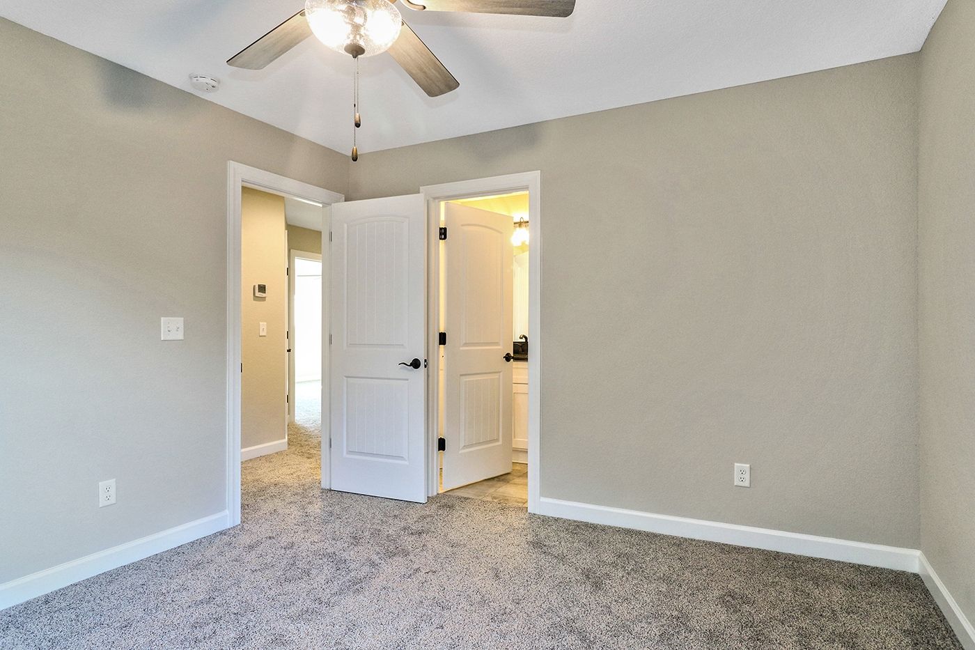 An empty bedroom with a ceiling fan and a carpeted floor.