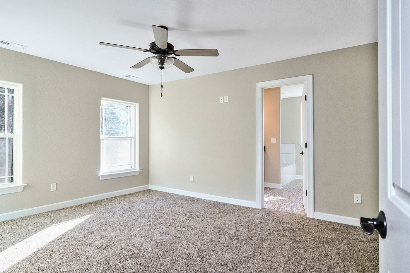 An empty bedroom with a ceiling fan and two windows.