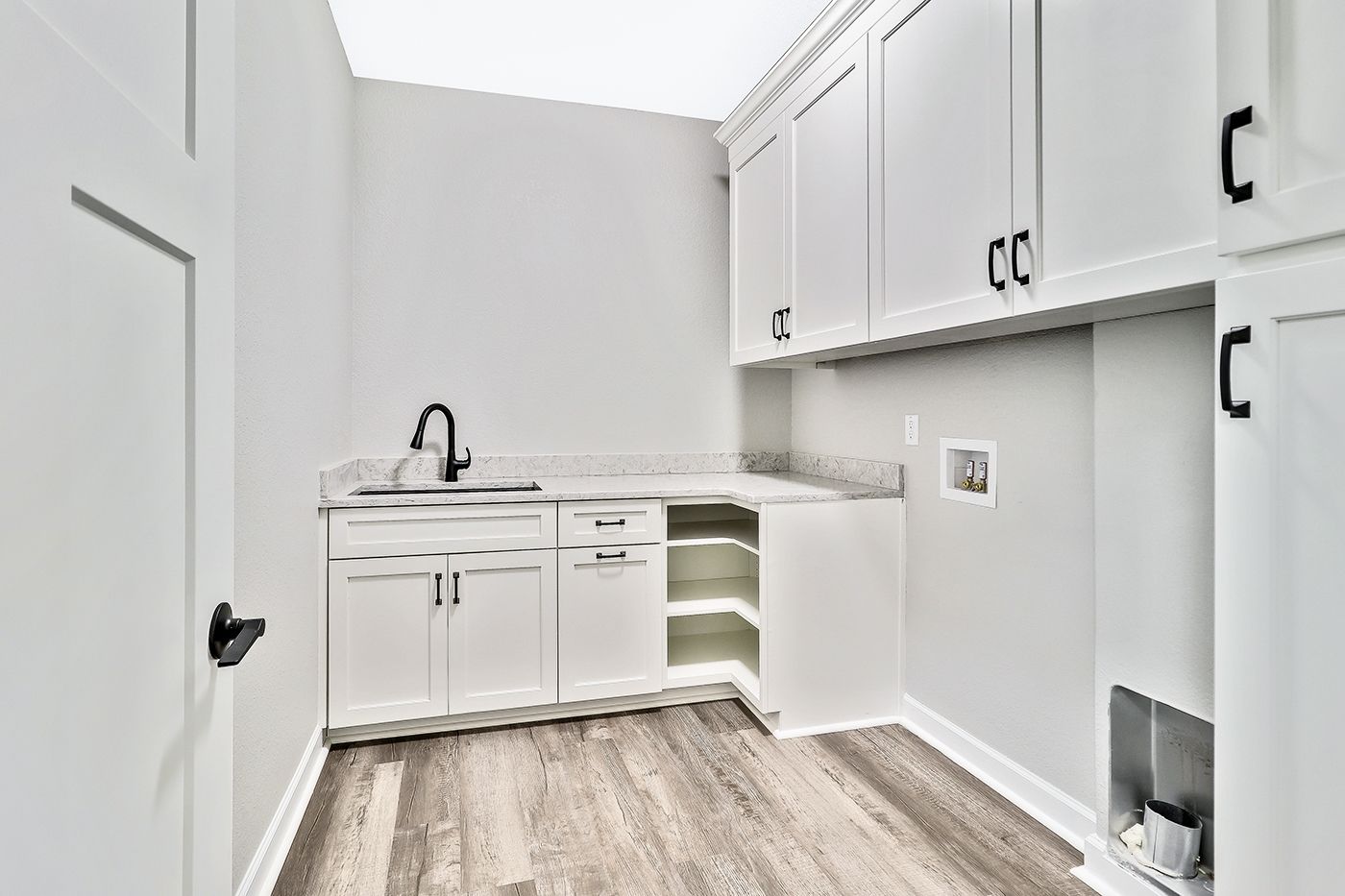 A laundry room with white cabinets , hardwood floors , and a sink.