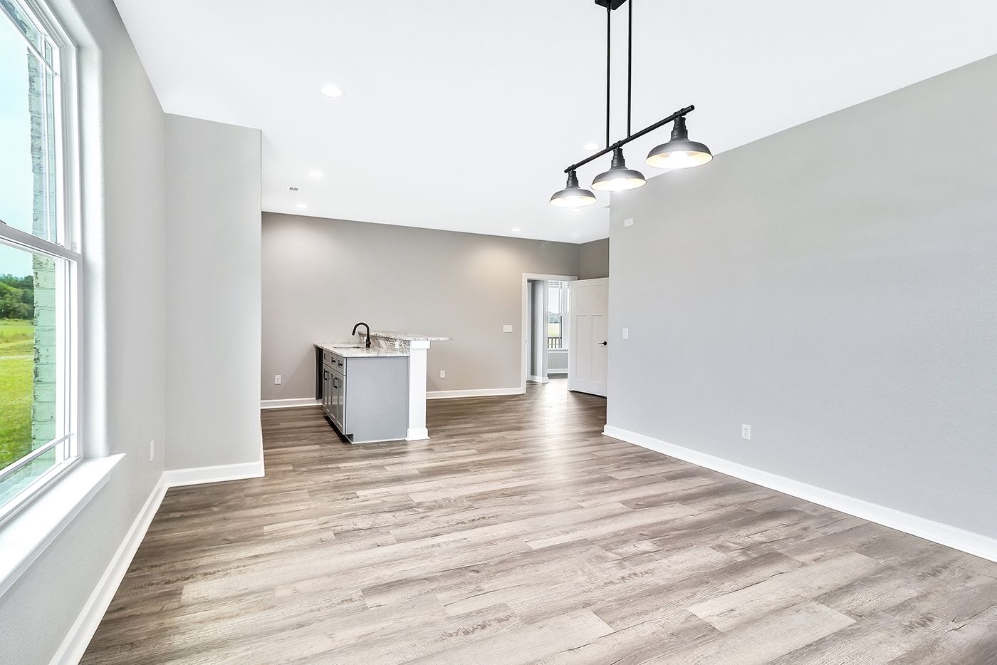 An empty living room with hardwood floors and a kitchen in the background.