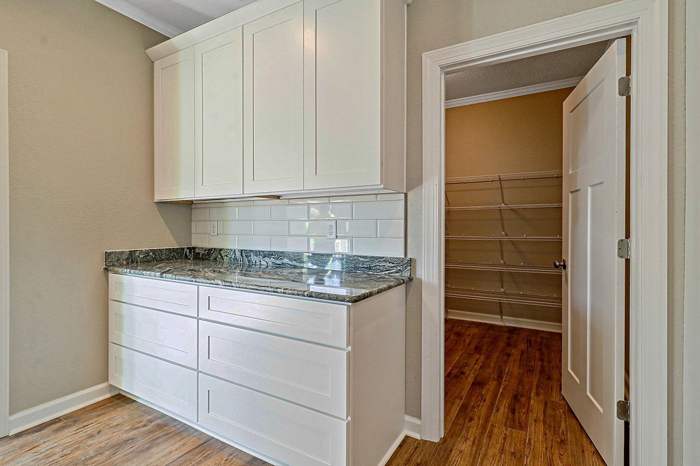 A kitchen with white cabinets and granite counter tops and a walk in pantry.