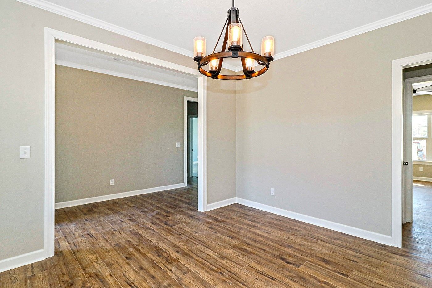 An empty dining room with hardwood floors and a chandelier hanging from the ceiling.
