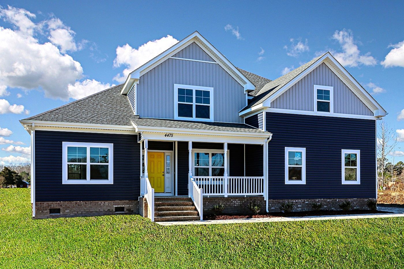 A blue and white house with a yellow door and porch is sitting on top of a lush green field.