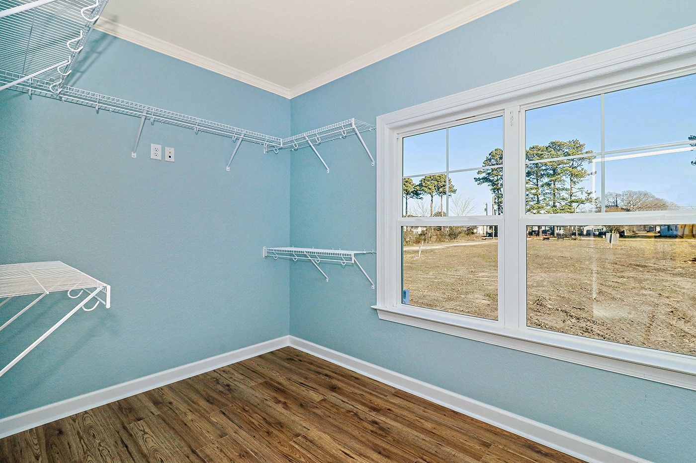 An empty walk in closet with a large window and wooden floors.