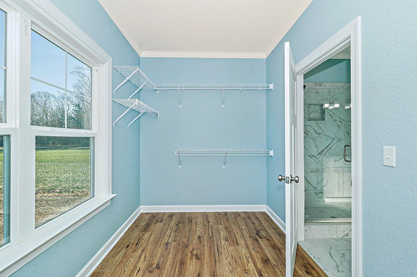 An empty walk in closet with blue walls and hardwood floors.