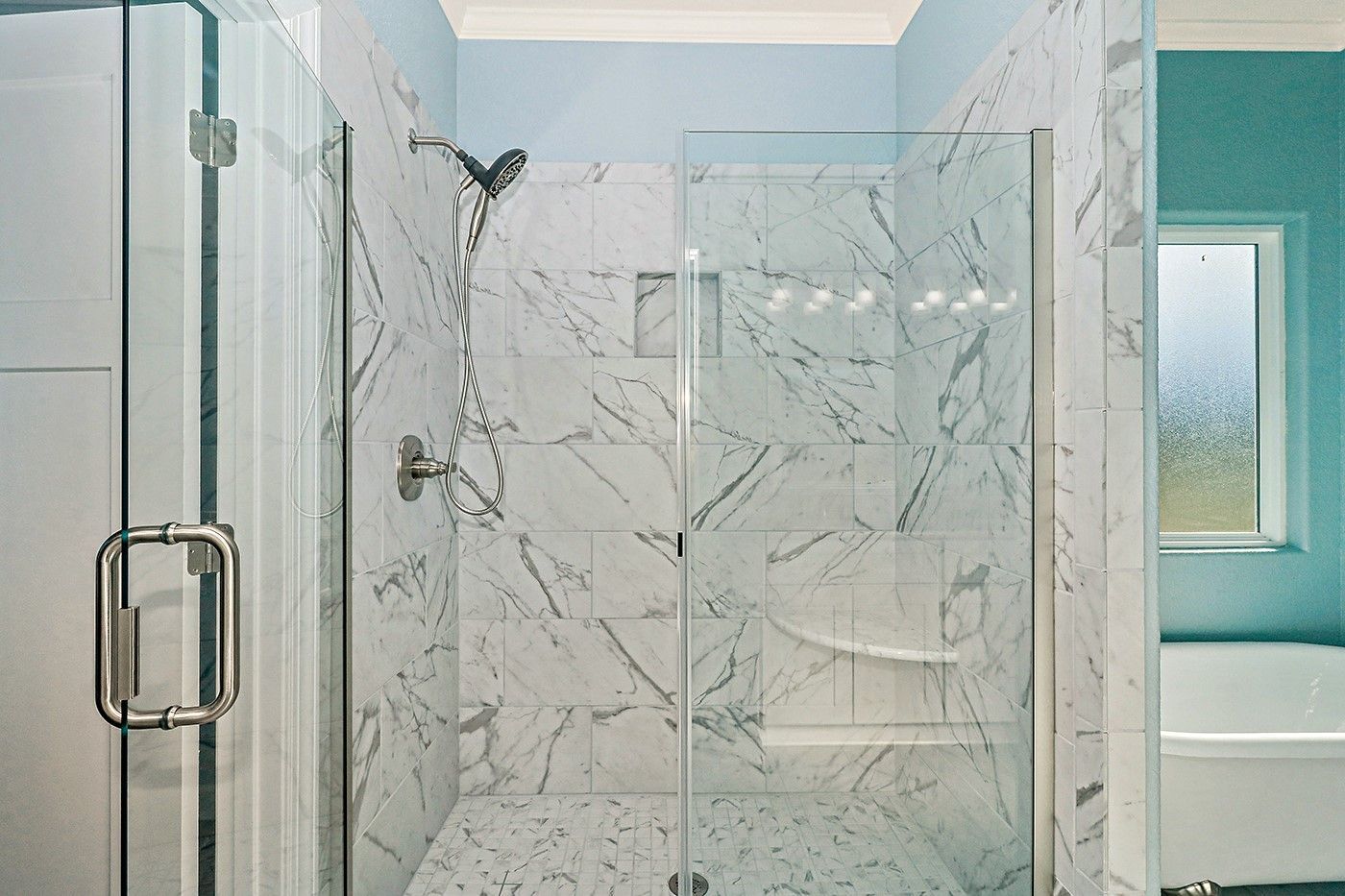 A bathroom with marble tiles and a walk in shower with a glass door.