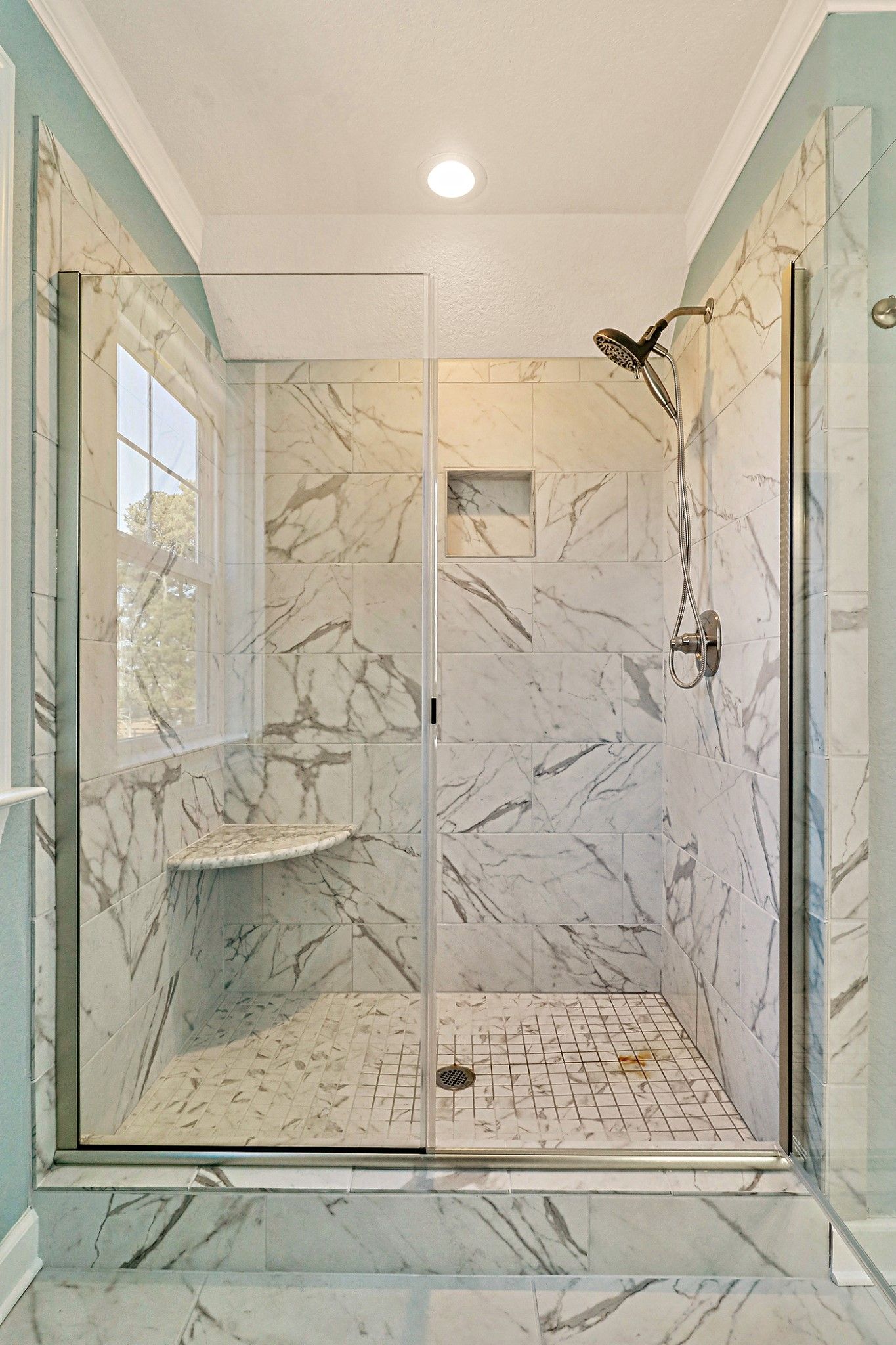 A bathroom with marble tiles and a walk in shower with a glass door.