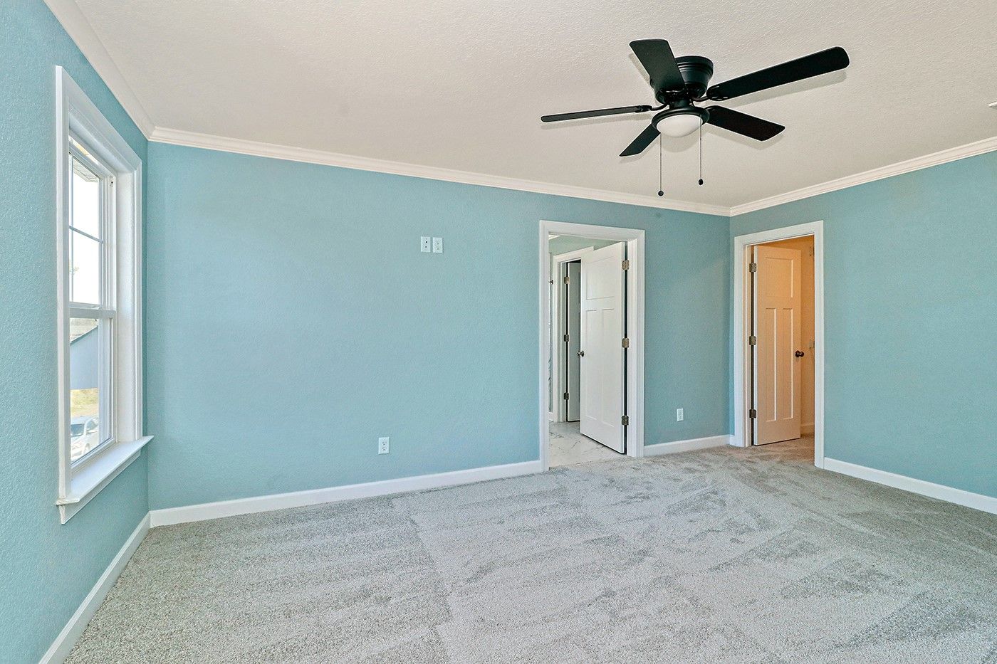 An empty bedroom with blue walls and a ceiling fan