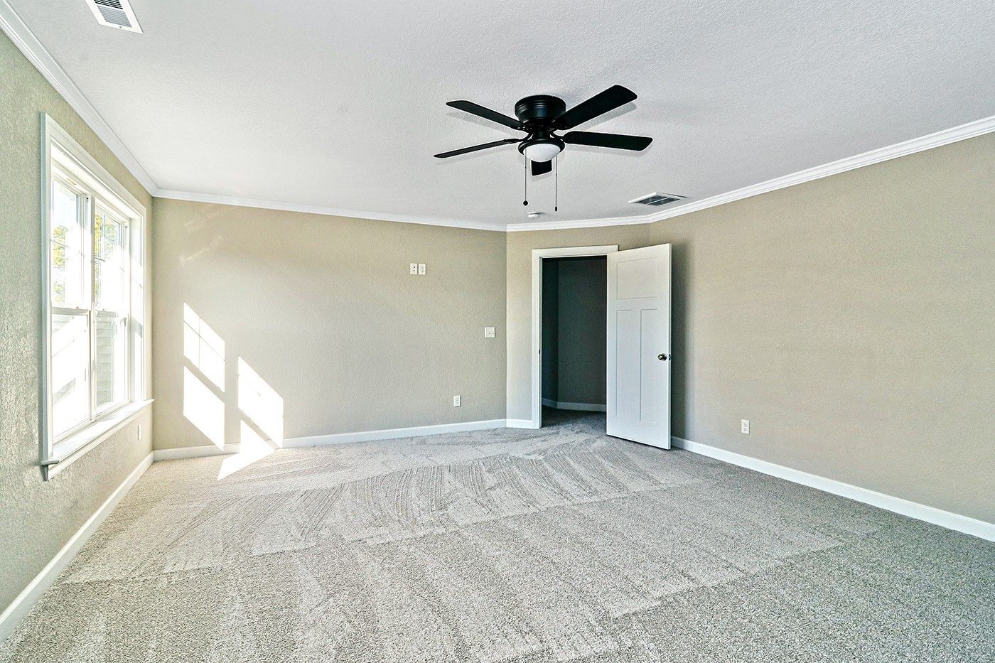 An empty bedroom with a ceiling fan and a carpeted floor.