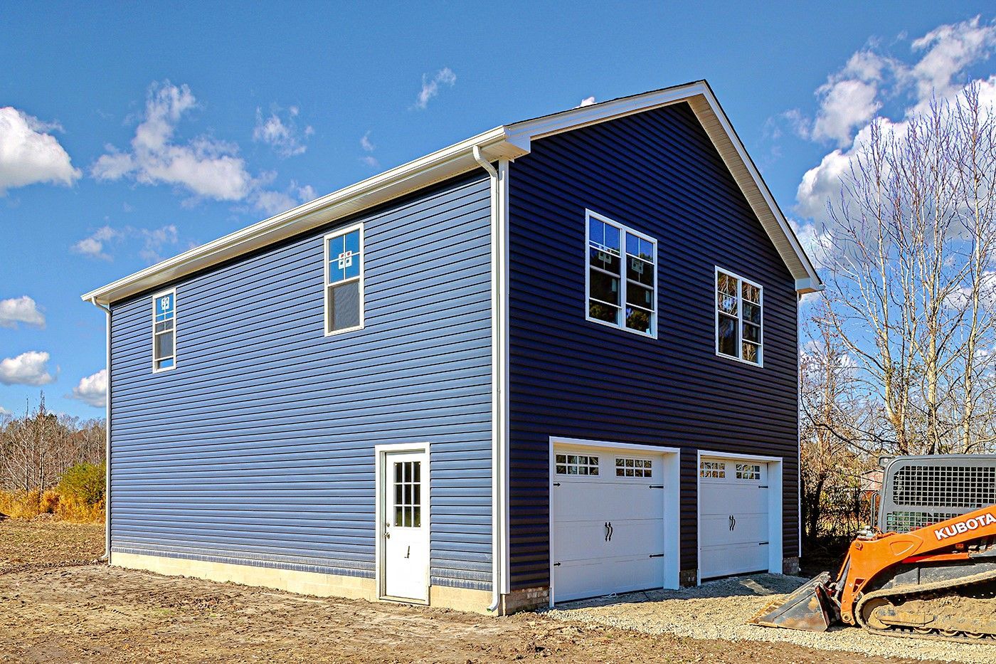 A large blue garage with two garage doors and a bulldozer in front of it.