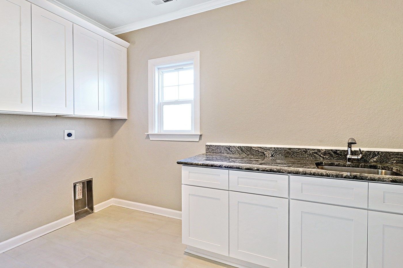 A laundry room with white cabinets , granite counter tops , and a window.