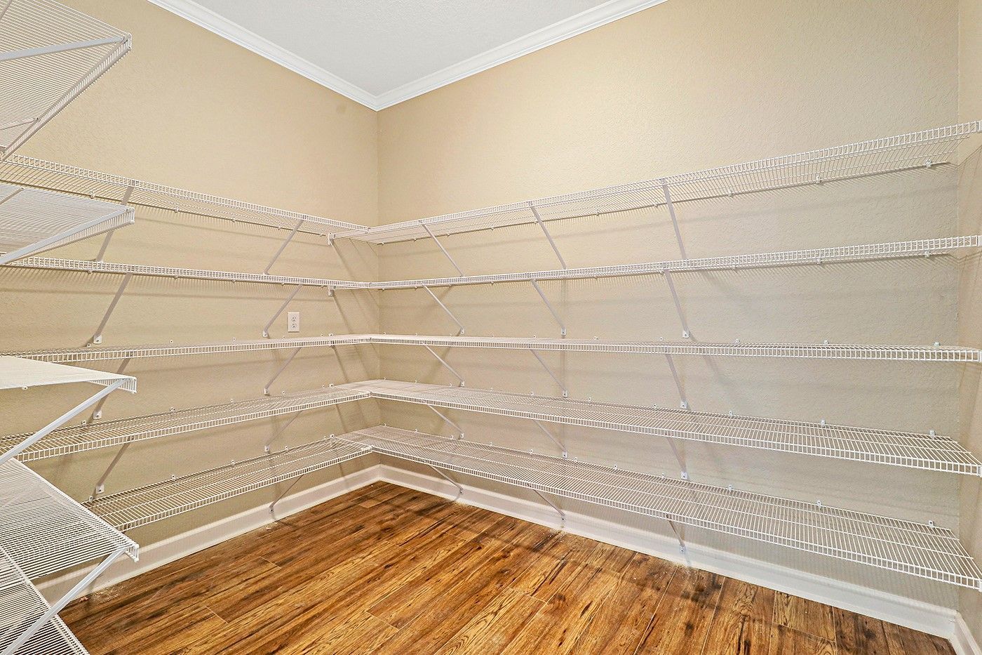 An empty walk in closet with wooden floors and white shelves.