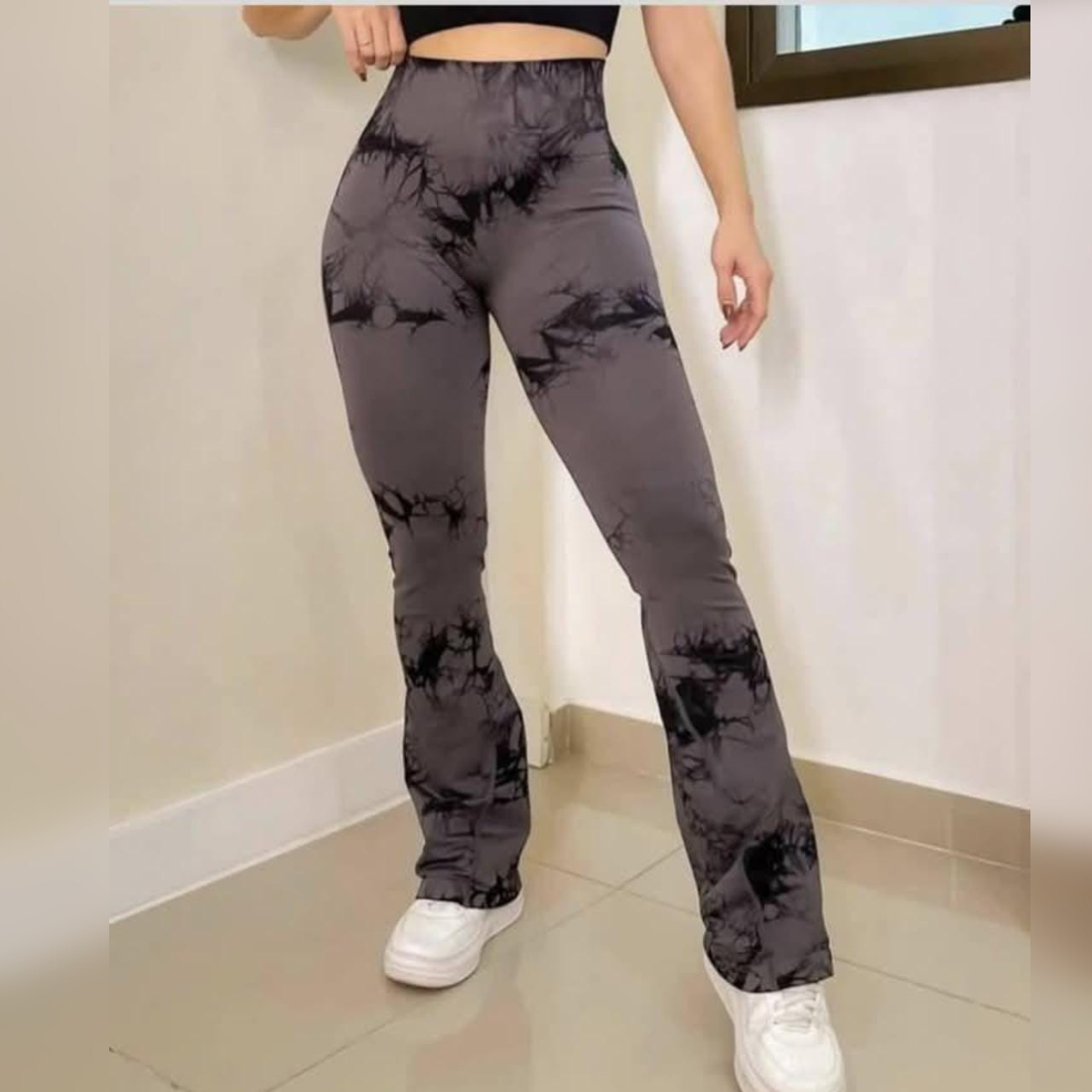 Mujer con pantalones acampanados con efecto tie-dye y zapatillas blancas en una habitación, haciendo una pose.