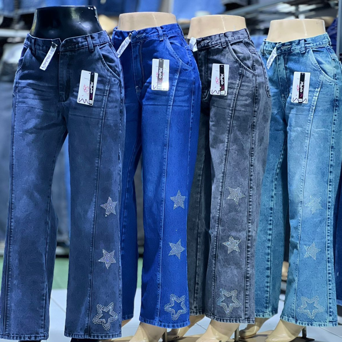 Cinco pares de jeans de mezclilla azul, cada uno con estrellas de diamantes de imitación y lavados variados, sobre maniquíes.