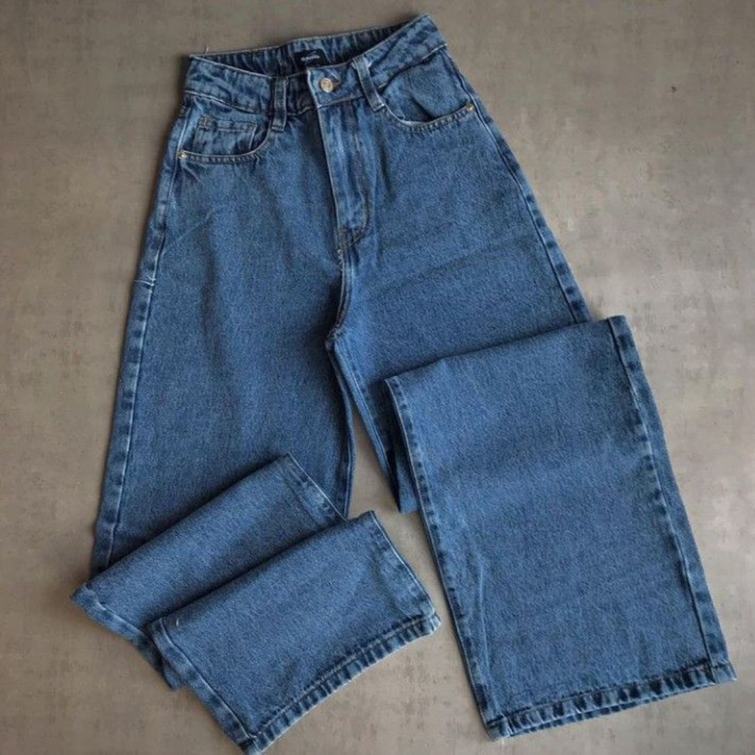 Pantalones vaqueros de pierna ancha de mezclilla azul sobre una superficie gris.
