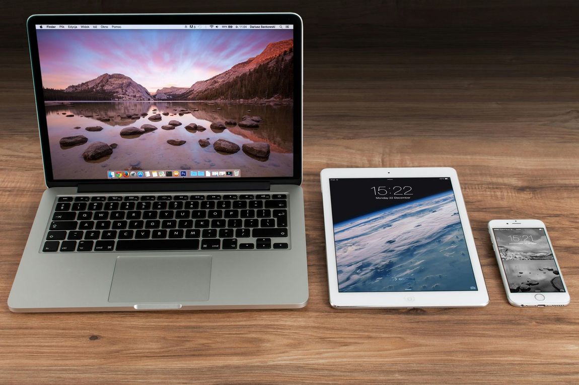 Laptop, tablet, and smartphone on a wooden surface, displaying different screens.