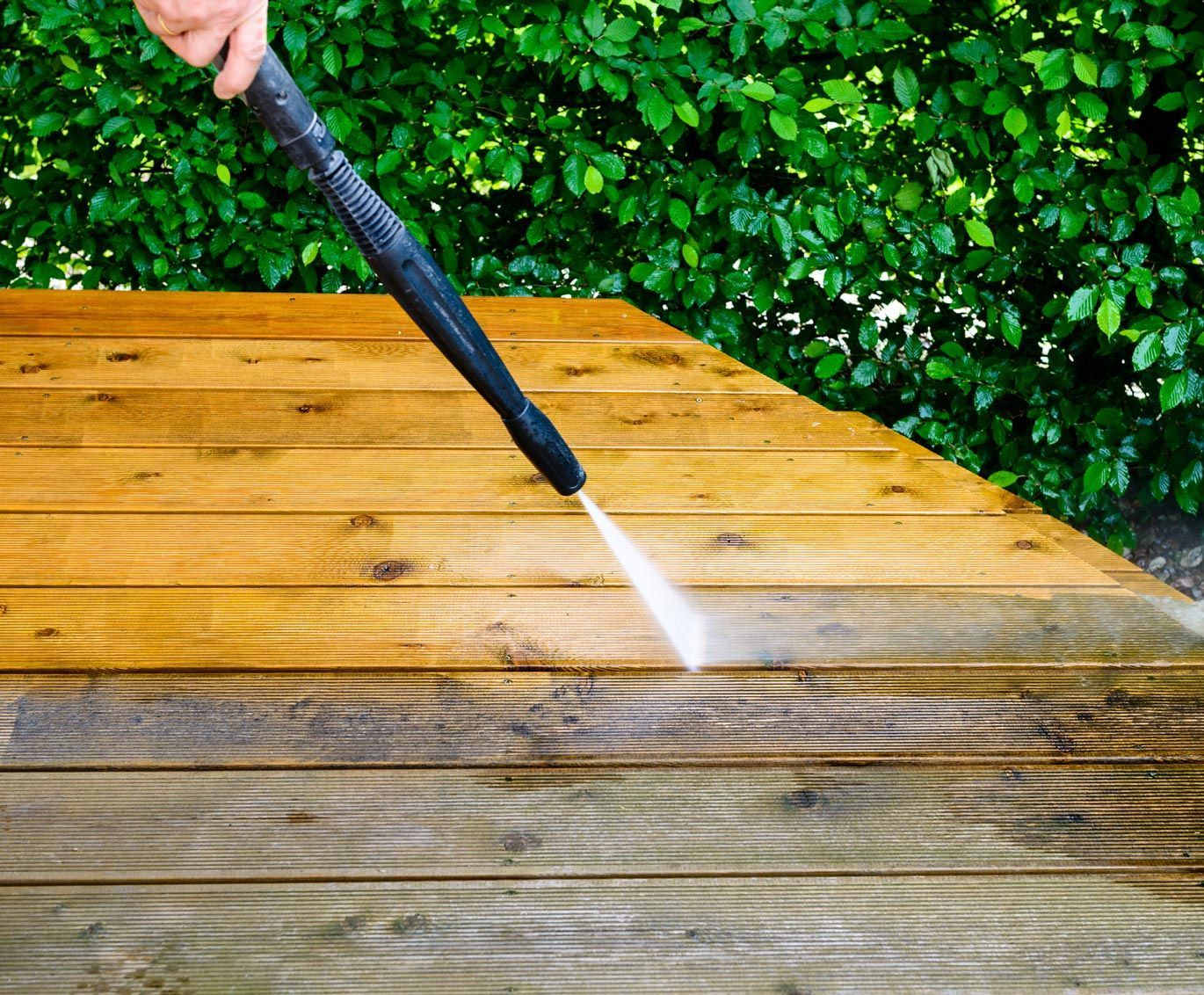 Pressure washing a wooden deck, removing dirt and grime.