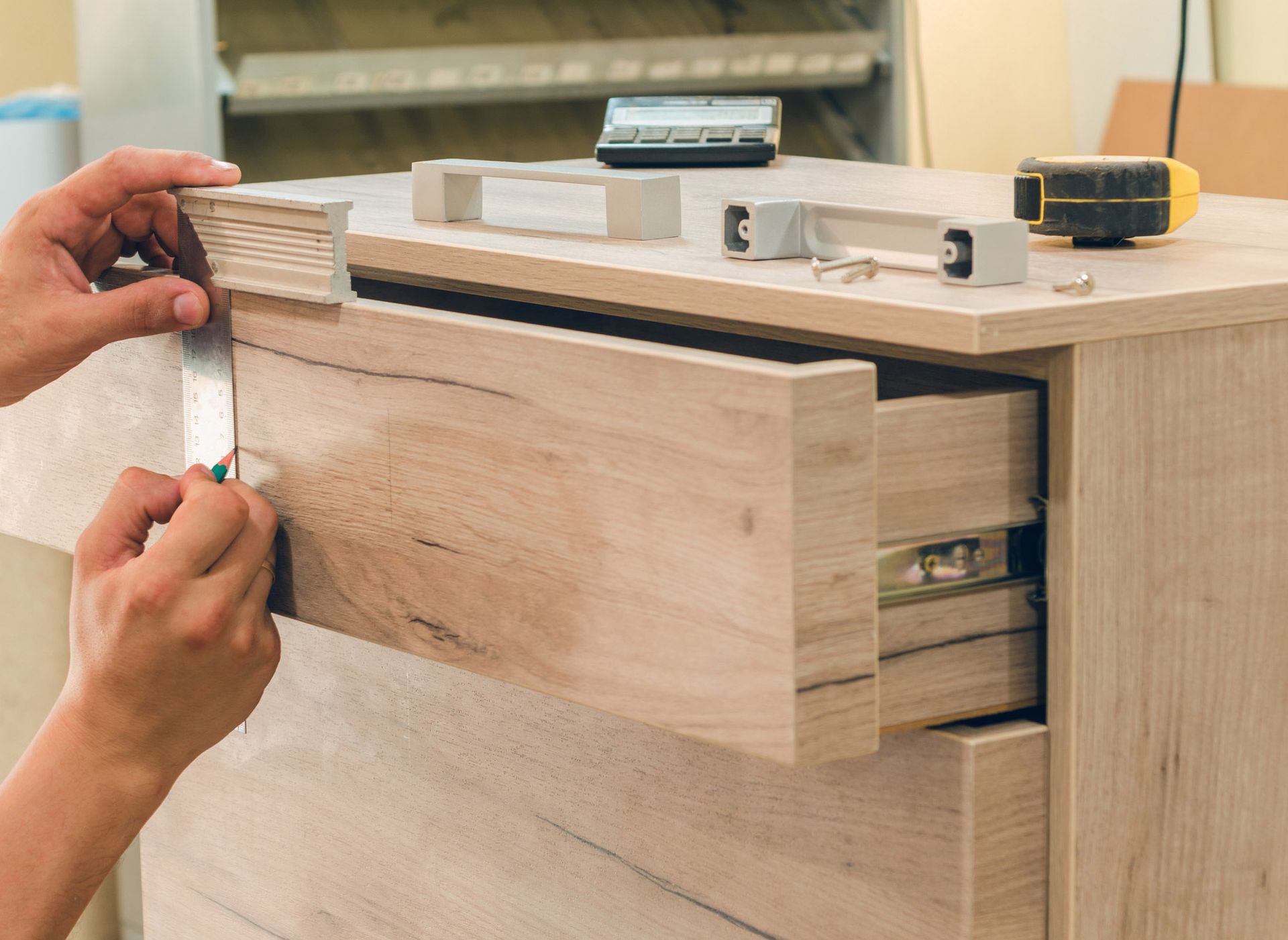 Person measuring and attaching hardware to a wooden drawer, preparing it for installation.