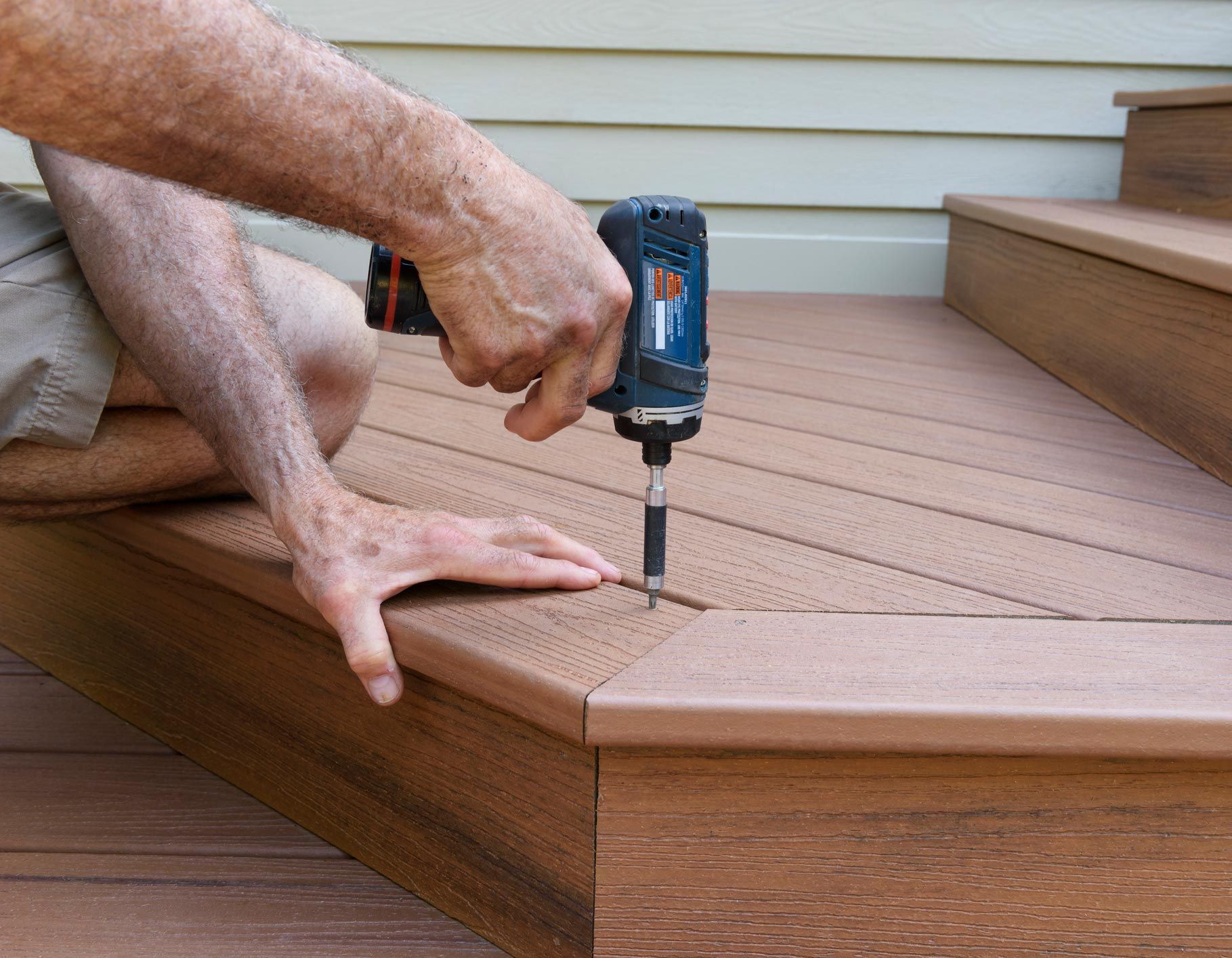 Person uses a drill to fasten a screw on a brown composite deck.