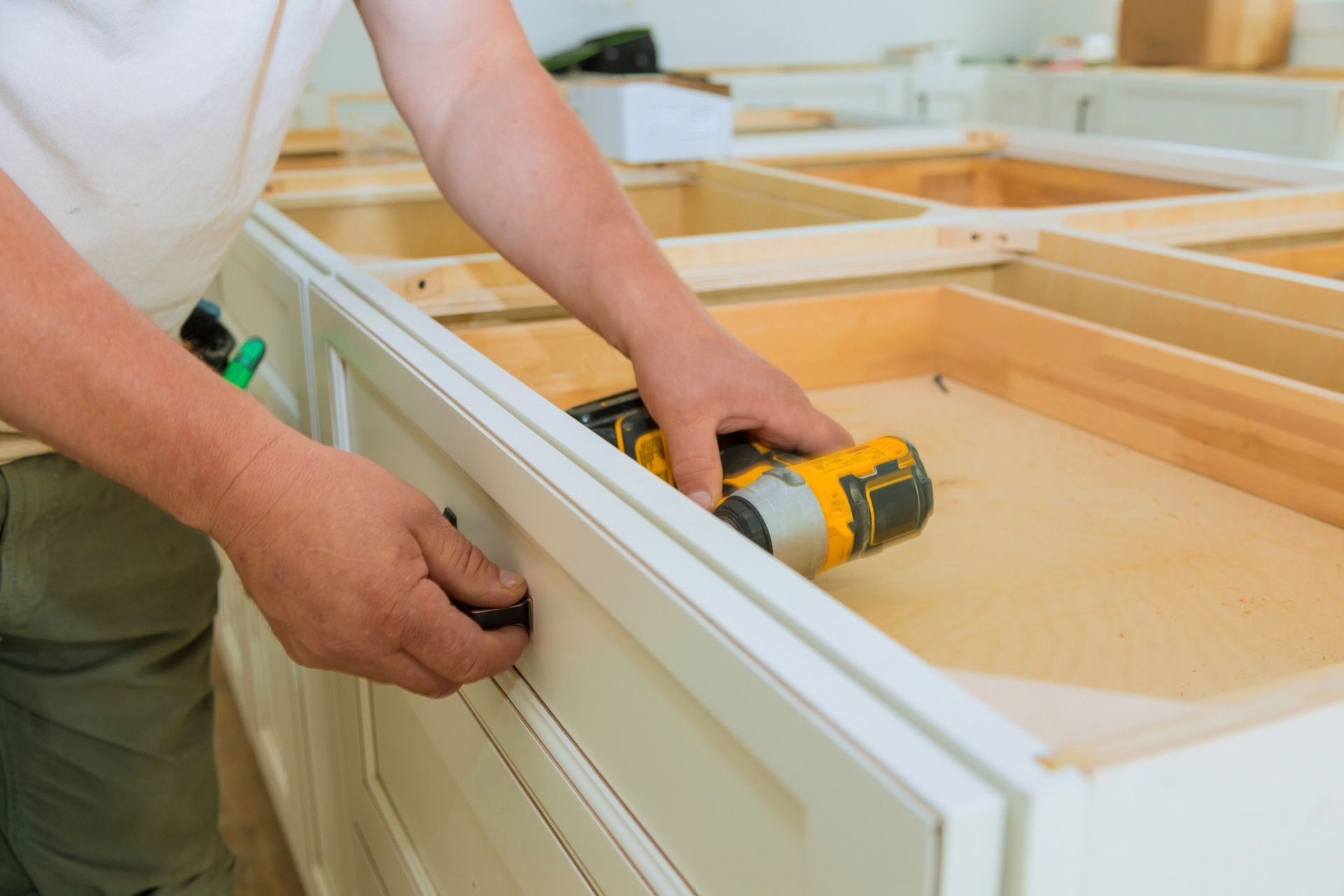 Person installing a cabinet door handle with a power drill in a kitchen.