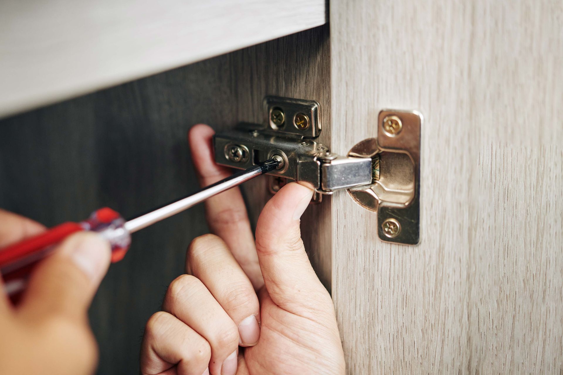 A person using a screwdriver to adjust a cabinet door hinge, indoors.