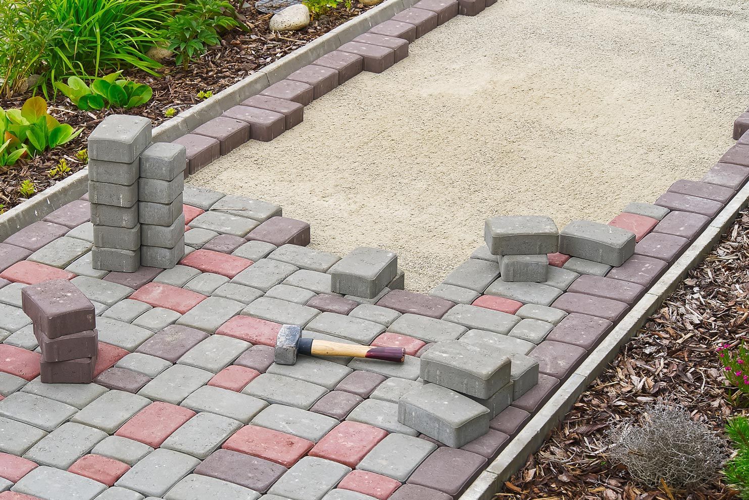 Pathway under construction with gray, red, and brown pavers, gravel base, and stacked blocks.