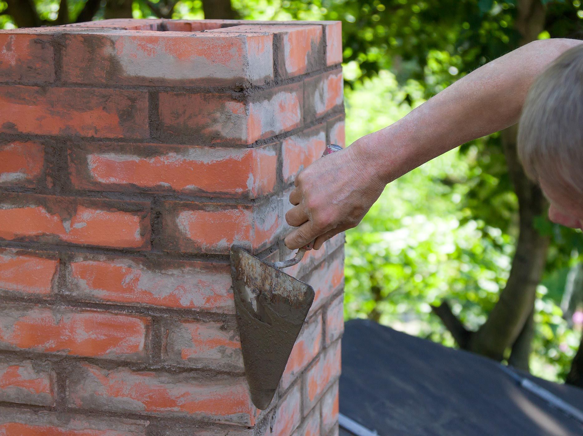 Person repairing a brick chimney, applying mortar with a trowel.