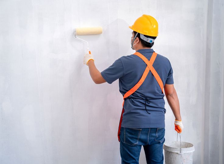 Person in safety gear paints a white wall with a roller.