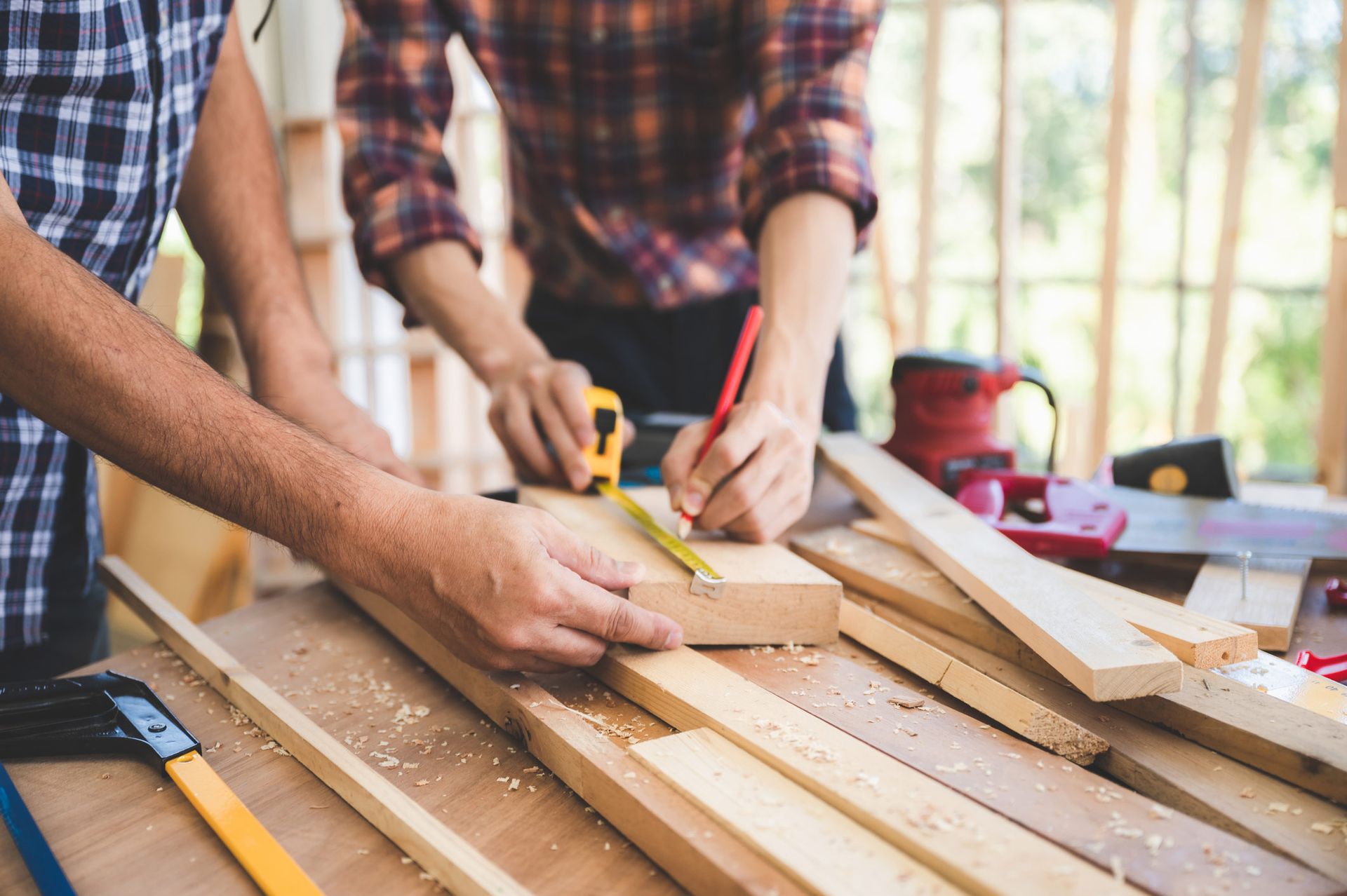 Two people working on woodworking project, measuring and marking wood with tools.