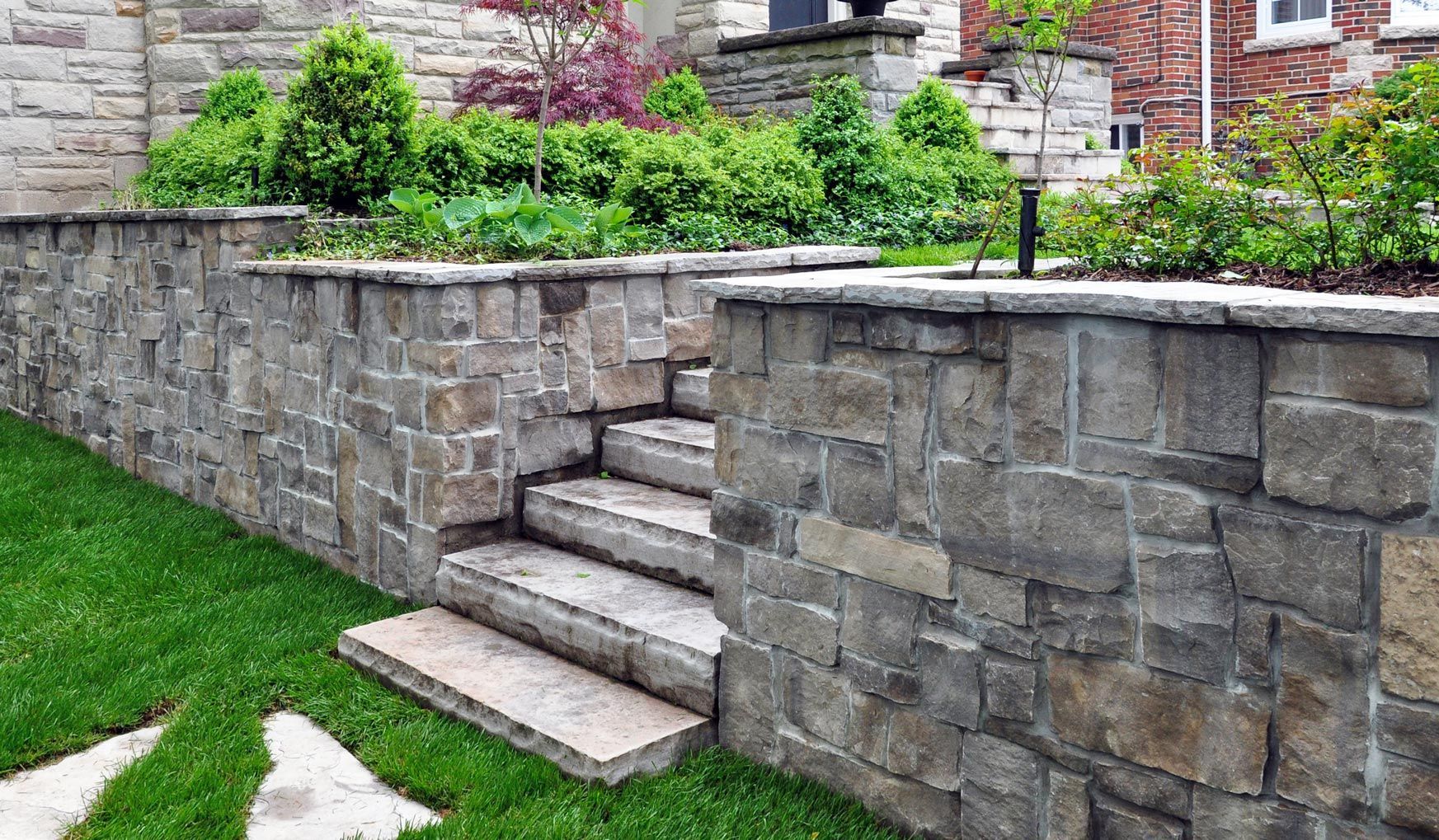 Stone retaining wall with steps, greenery, and a garden.
