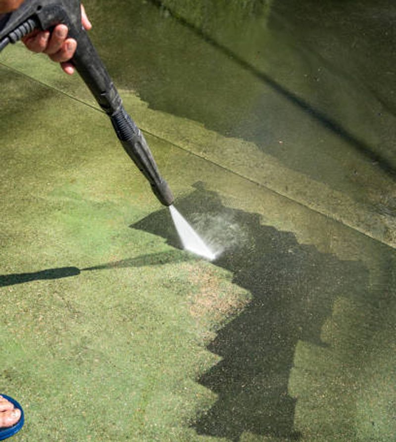 A person power washing a green surface, cleaning a dark path in the dirt.
