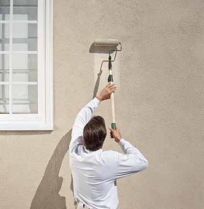 Man painting stucco exterior wall with roller.