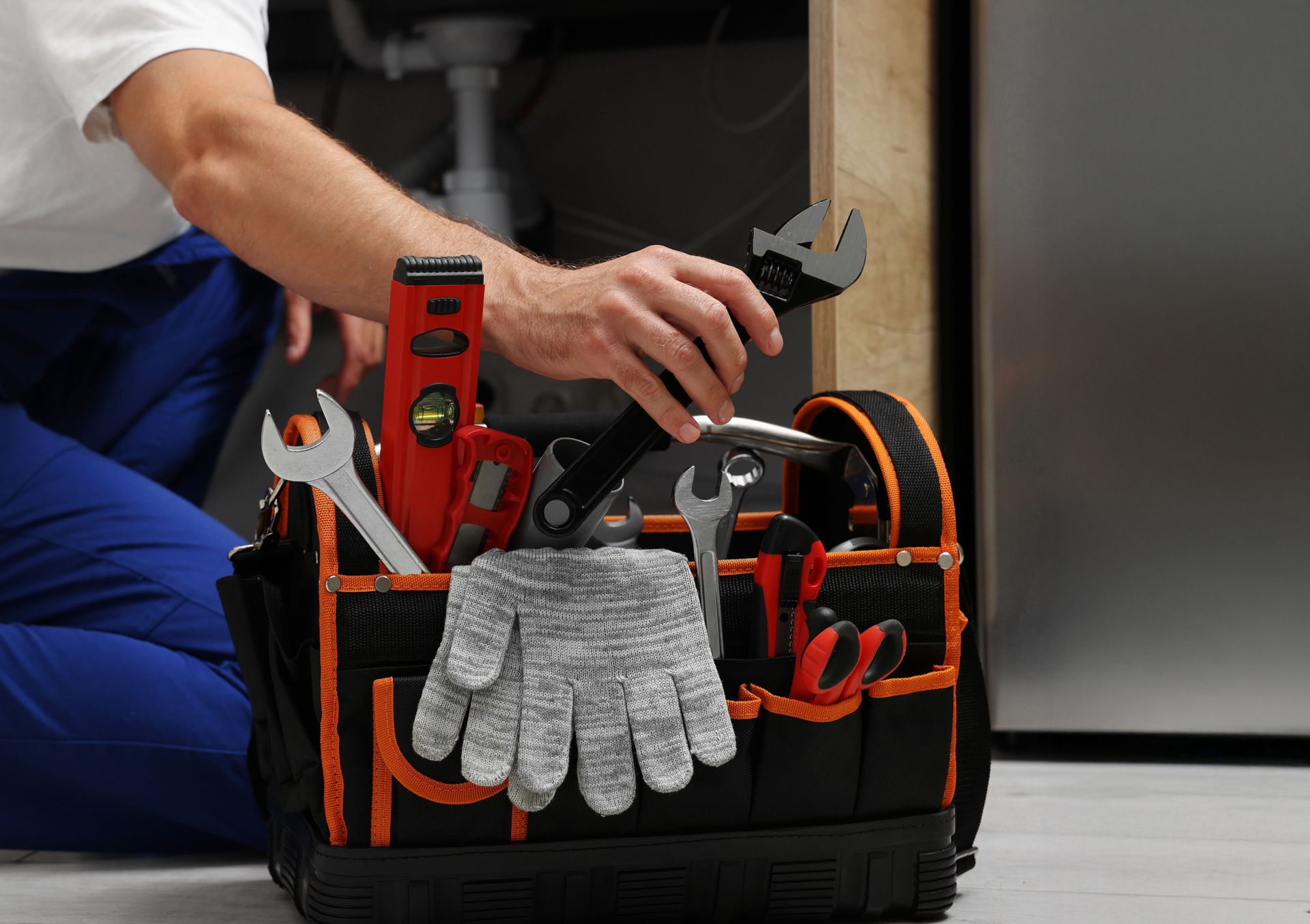 Plumber reaching into a black tool bag filled with tools, including a level and wrench.