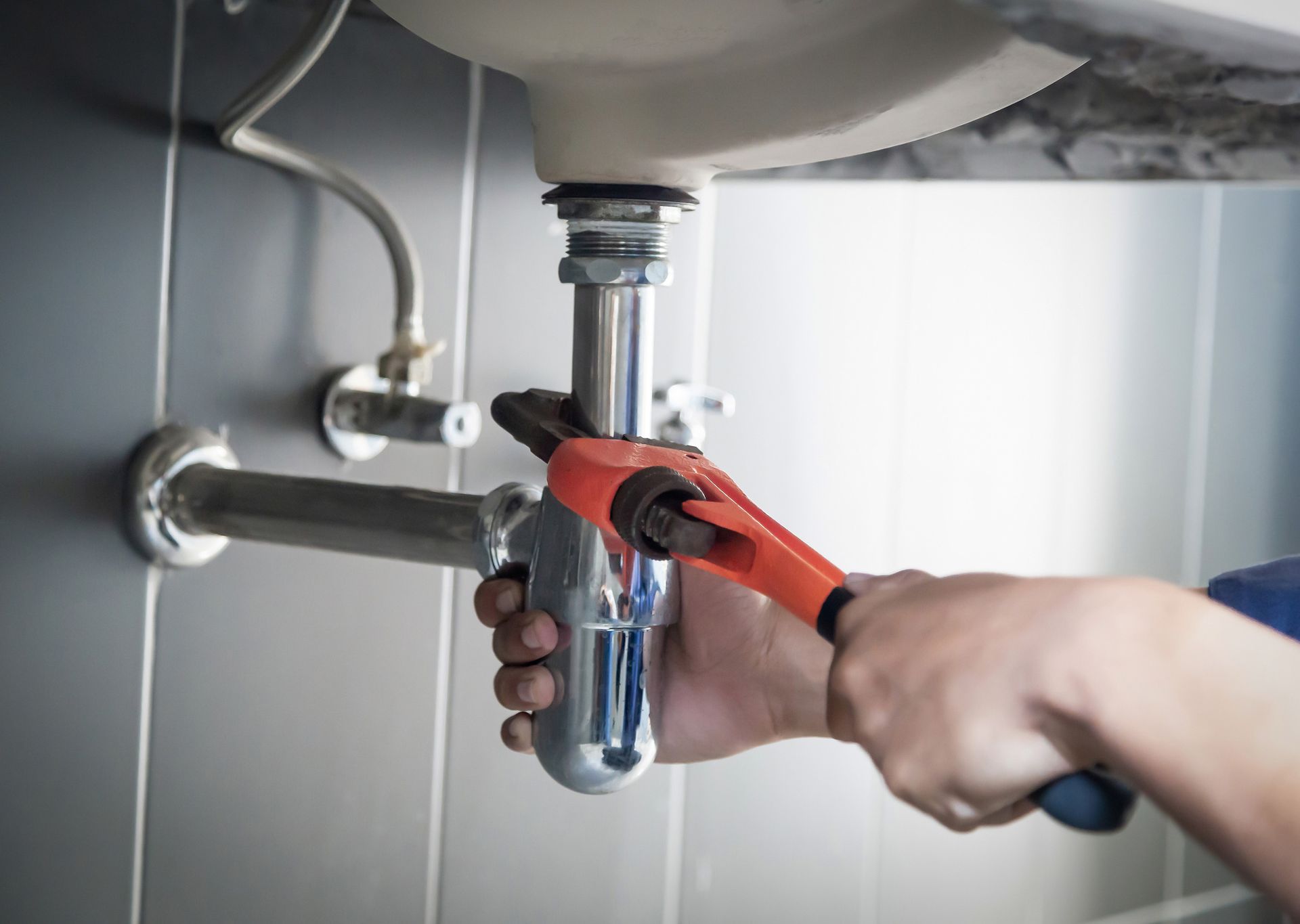 Plumber using a wrench to work on pipes under a bathroom sink.