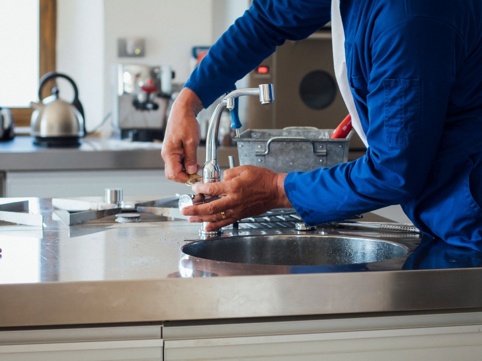 Person in blue washing dishes in a stainless steel sink in a kitchen.