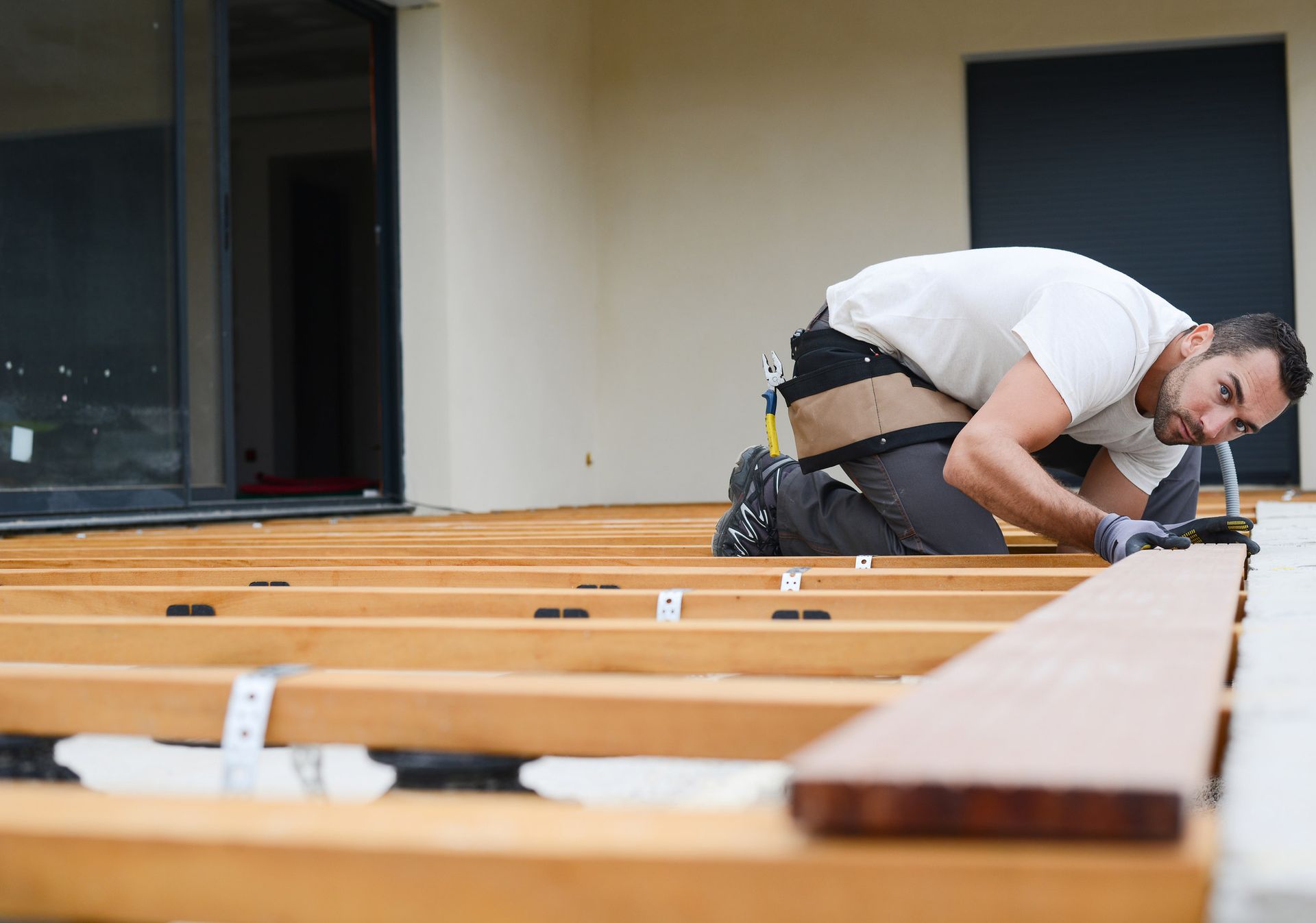 Man kneeling, installing wooden deck boards outdoors.