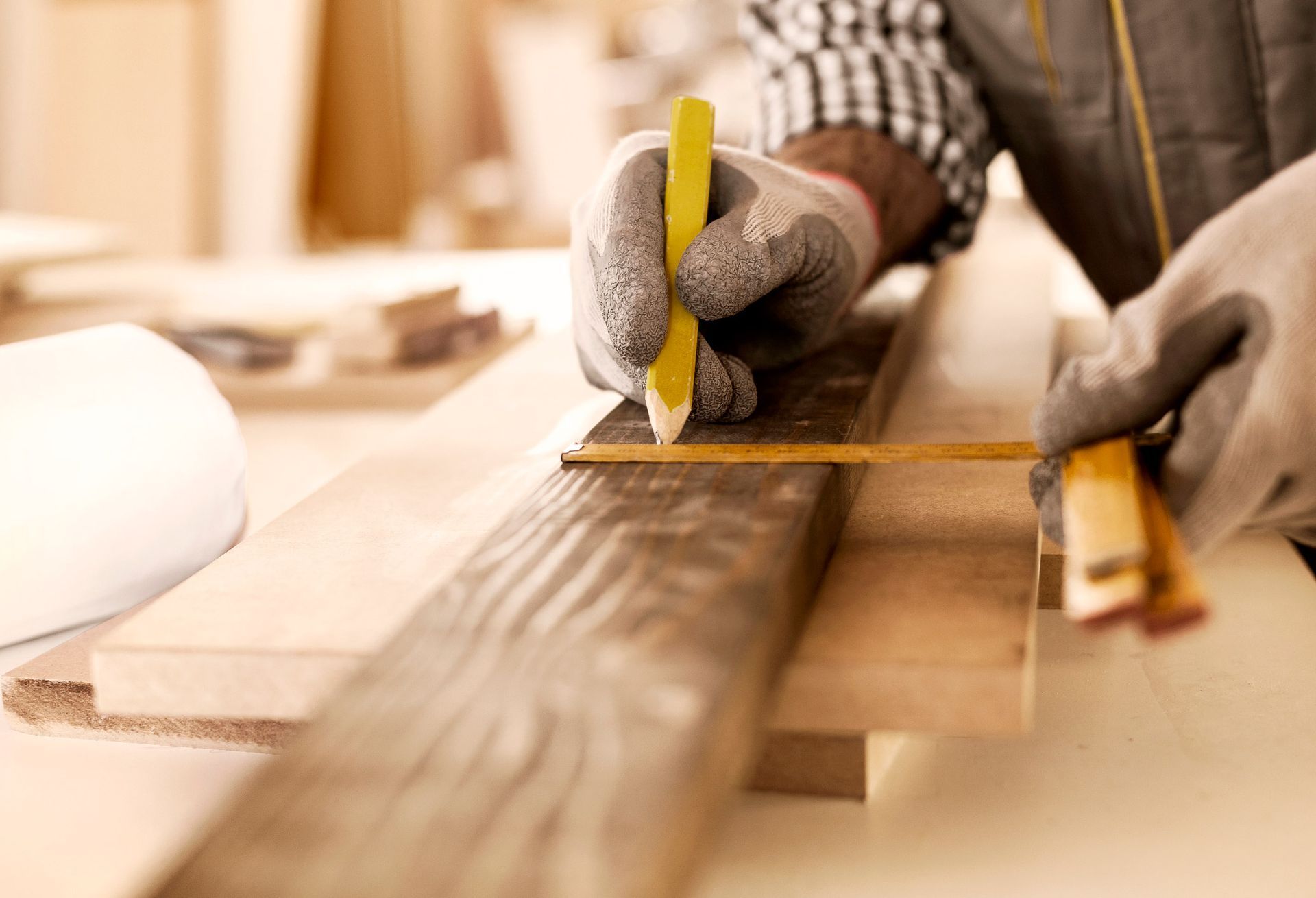 Carpenter measuring and marking wood with a pencil and ruler in a workshop.